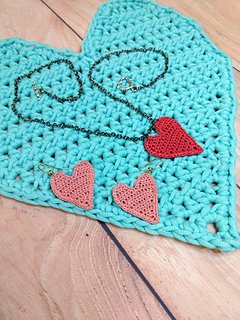 Heart shaped crocheted earrings and necklace placed on a crocheted heart shaped placemat.